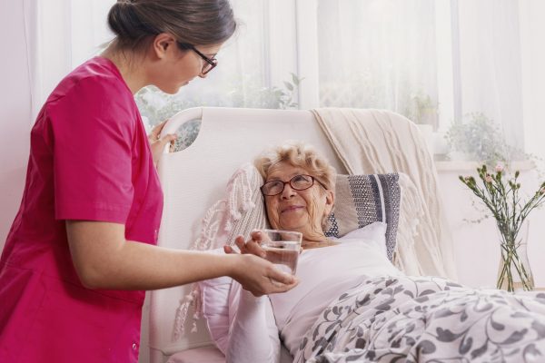 Beautiful young nurse serves tea to an elderly lady in a private nursing home